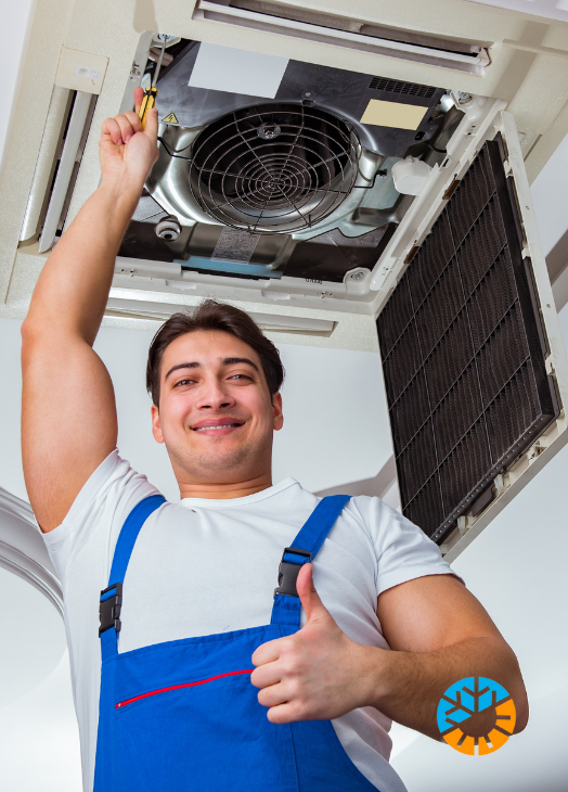 Técnico en uniforme azul dando un pulgar arriba mientras trabaja en un aire acondicionado en el techo.